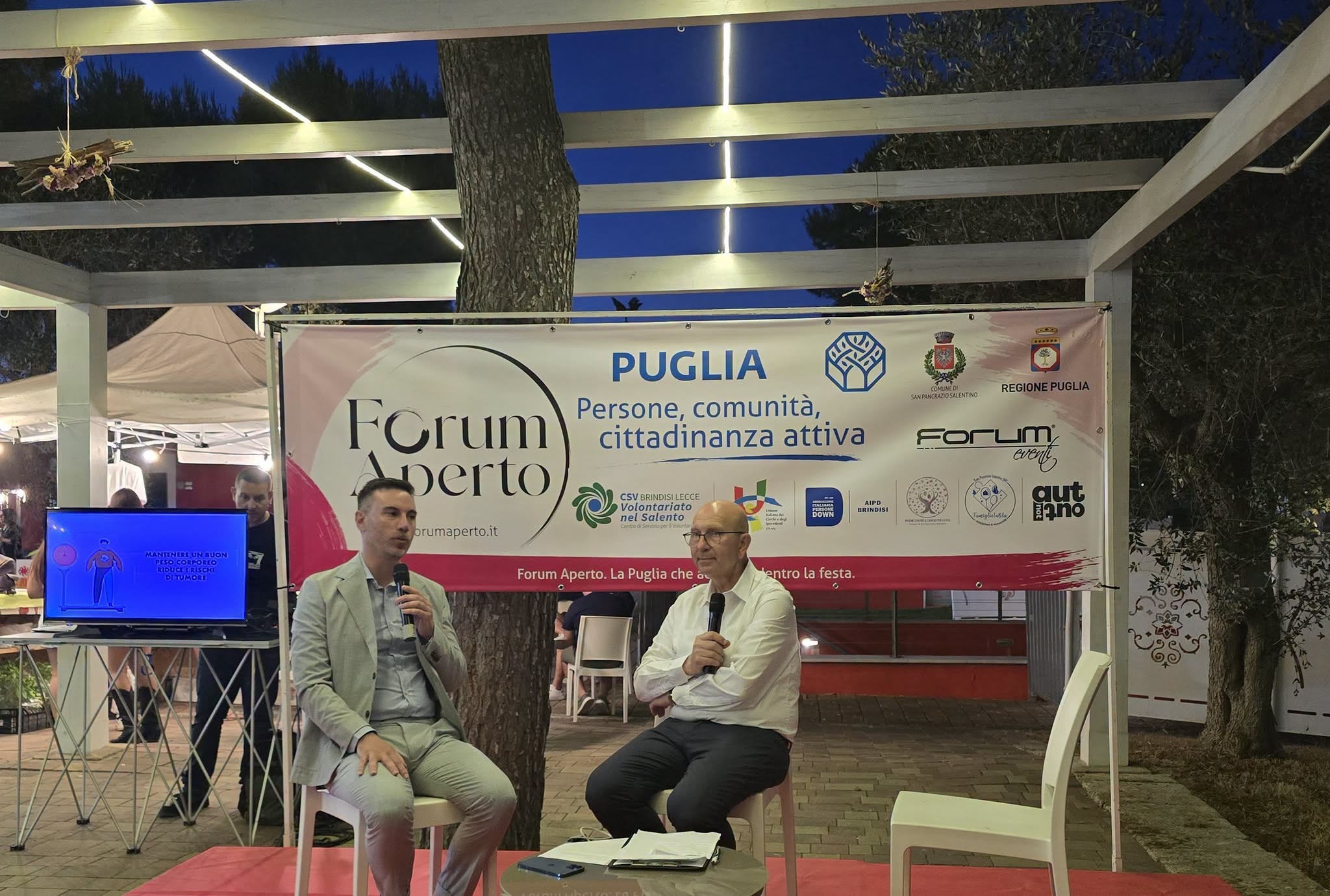 Il dott. Raffaele Quarta, ASL Brindisi, al talk del presidio salute con lo schermo delle infografiche sulla prevenzione