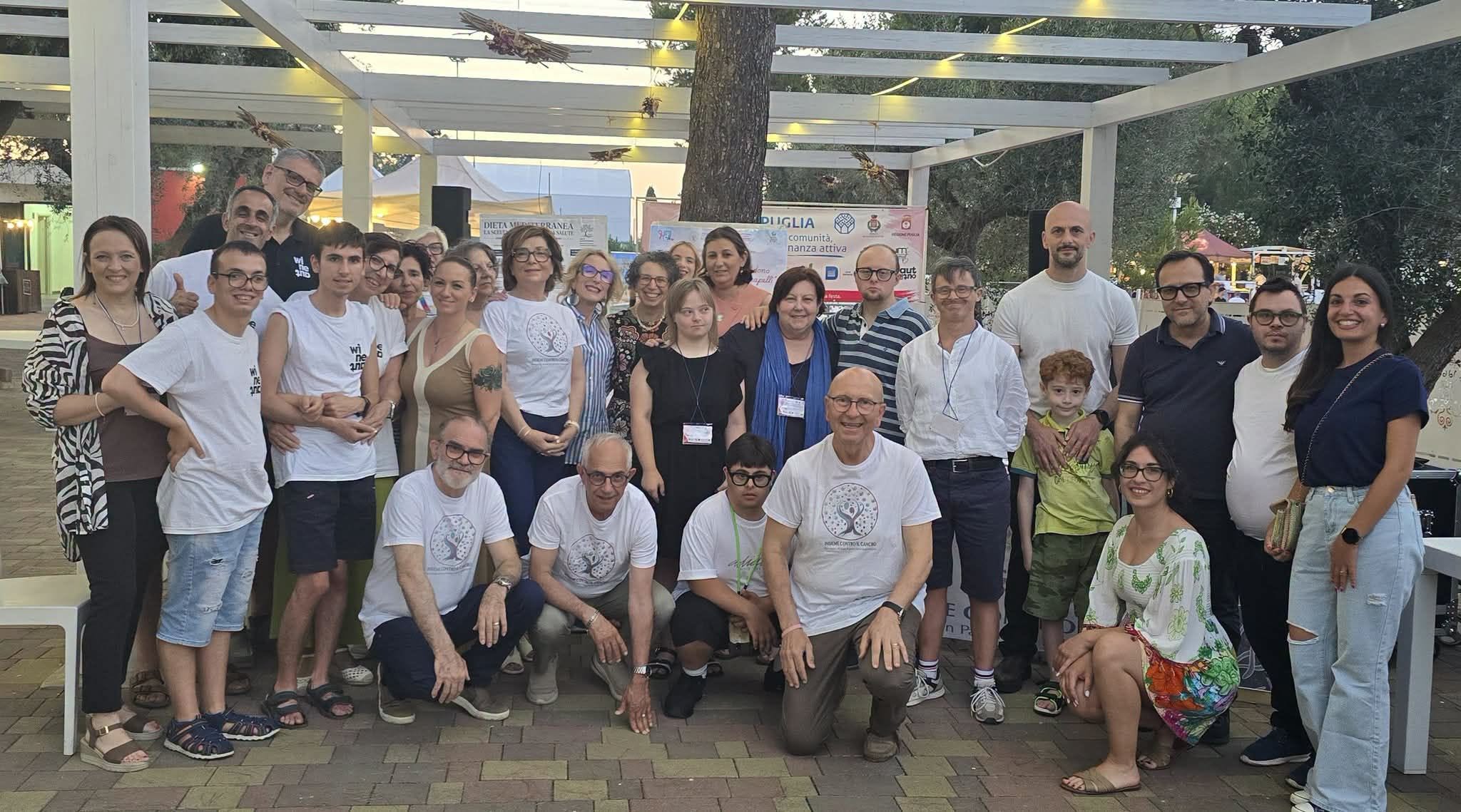 Grande foto di gruppo di volontari, associazioni e famiglie dell'area Forum Aperto sotto la pergola dei Giardini Forum Eventi